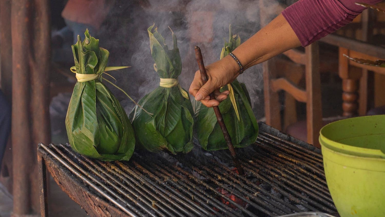 Hands folding tamales in bright green leaves